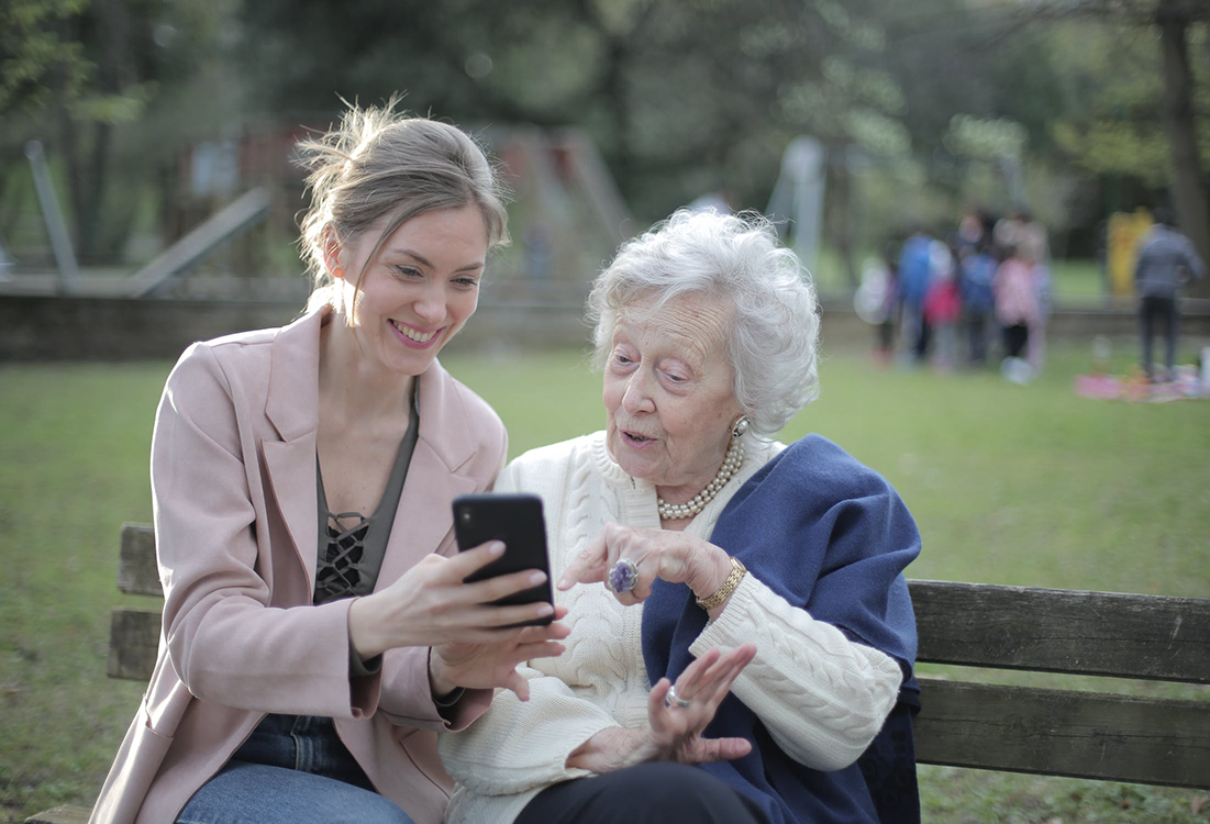 En yngre kvinna hjälper en äldre kvinna med mobiltelefon.